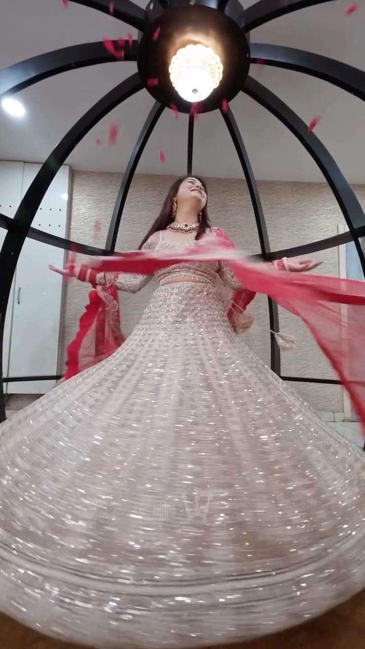 Bride twirling in a sparkling lehenga with red dupatta beneath a chandelier